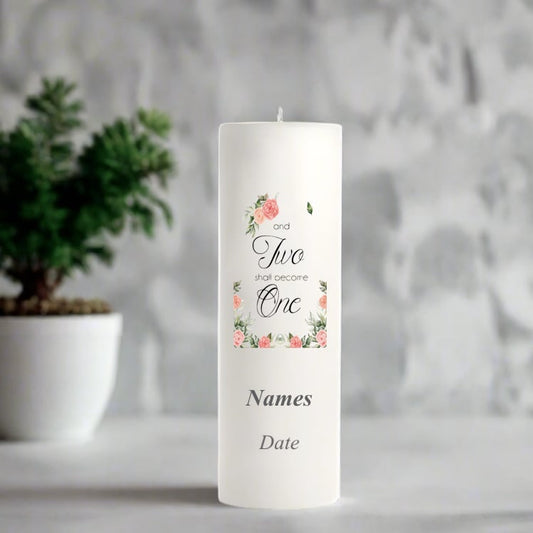 White wedding candle with floral design and text on a gray surface with a plant in the background