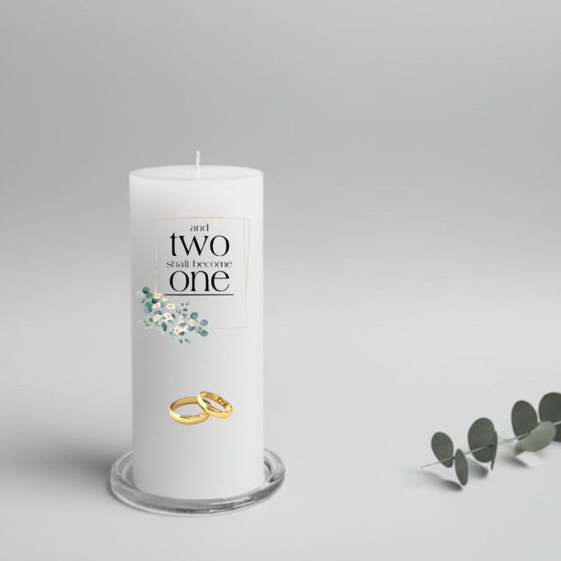 White wedding candle with 'and two shall become one' text, gold rings, and eucalyptus leaves 