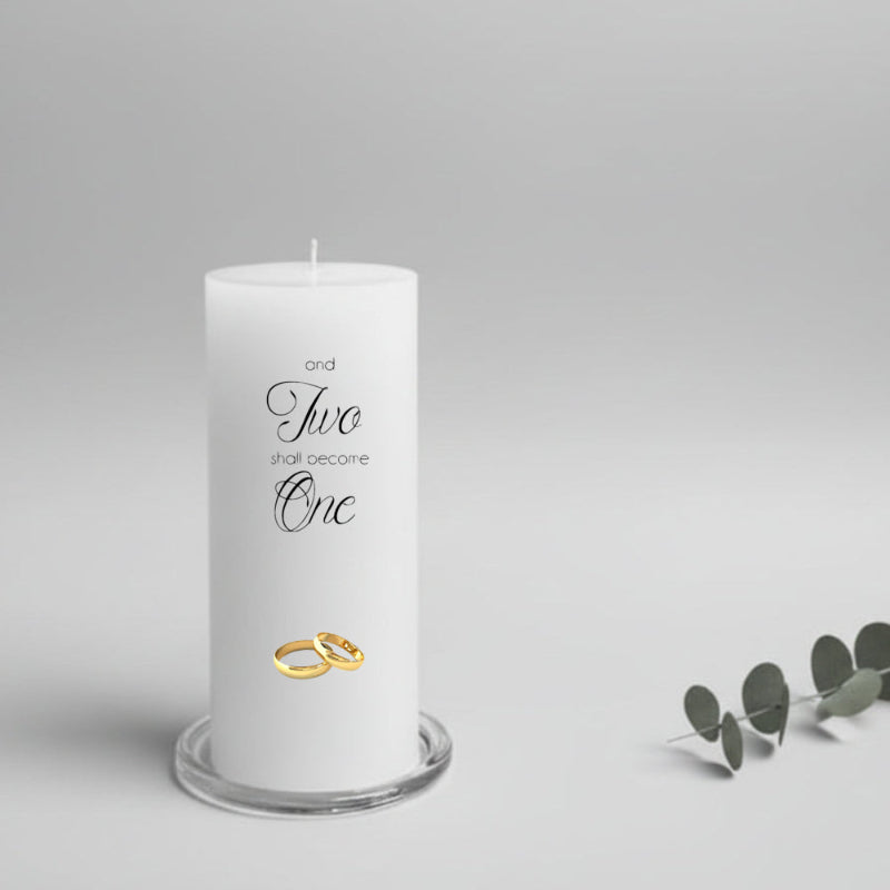 White candle with 'Two shall become One' text and gold rings, on a gray background