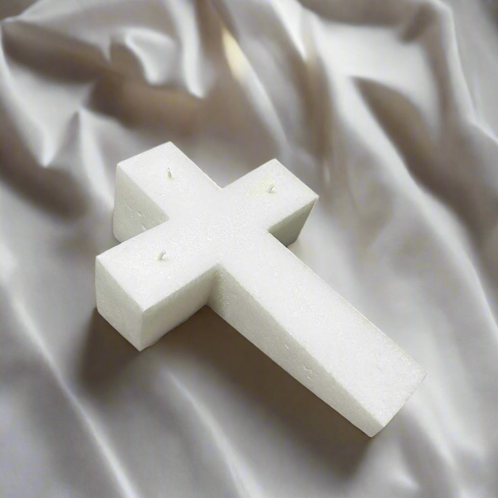 White cross-shaped candle on a silk material covered desk